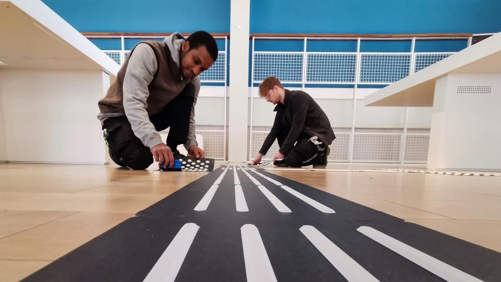 Zwei Männer montieren ein Bodenleitsystem in einer Sporthalle