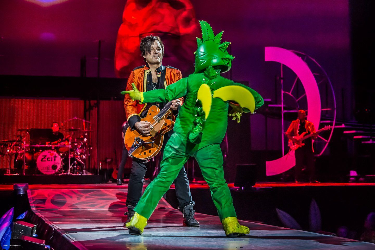 Der Drache Tabaluga tanzt vor einem E-Gitarren-Spieler.