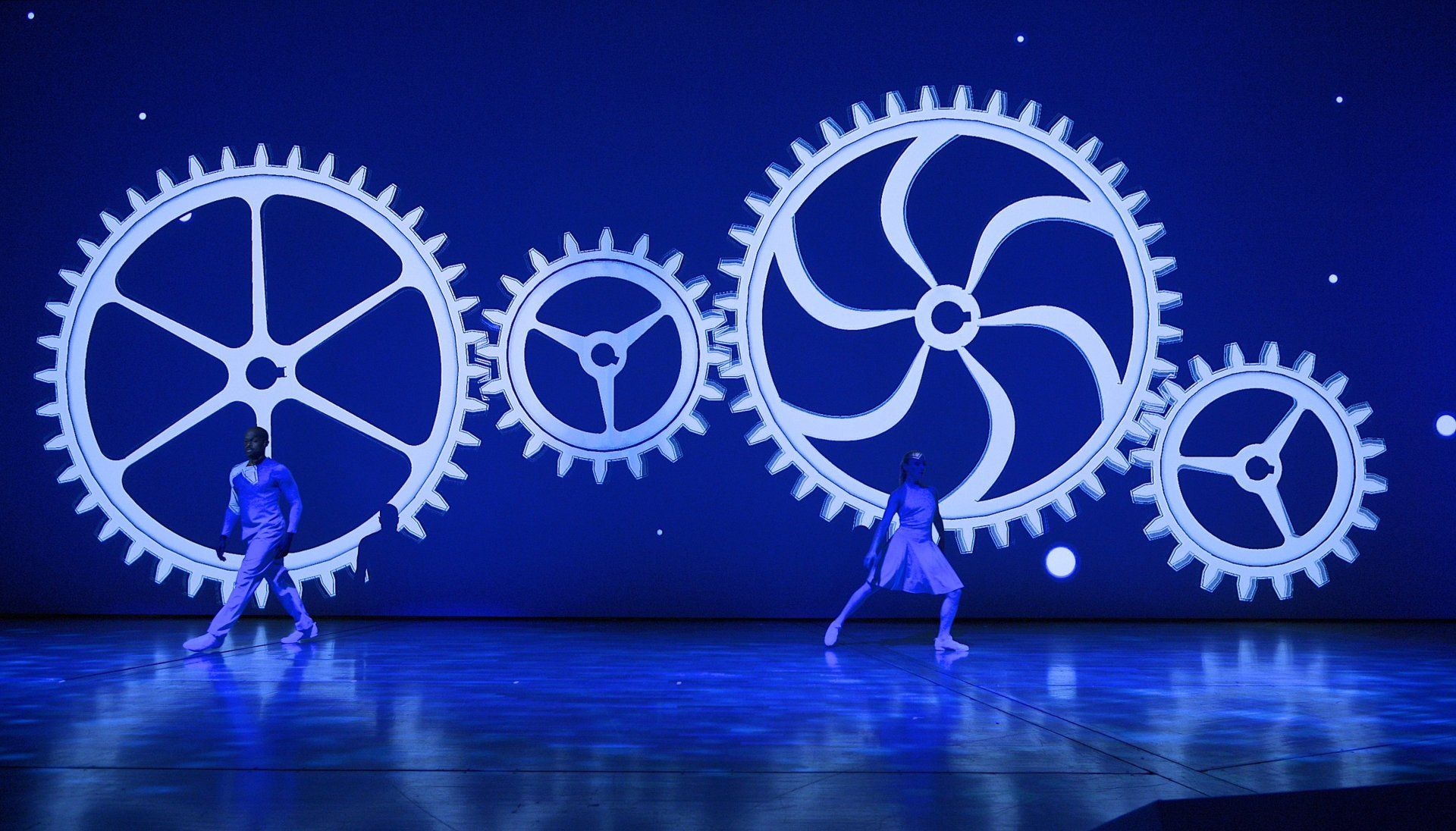 Zwei Tänzer auf blauer Bühne vor Zahnrädern
