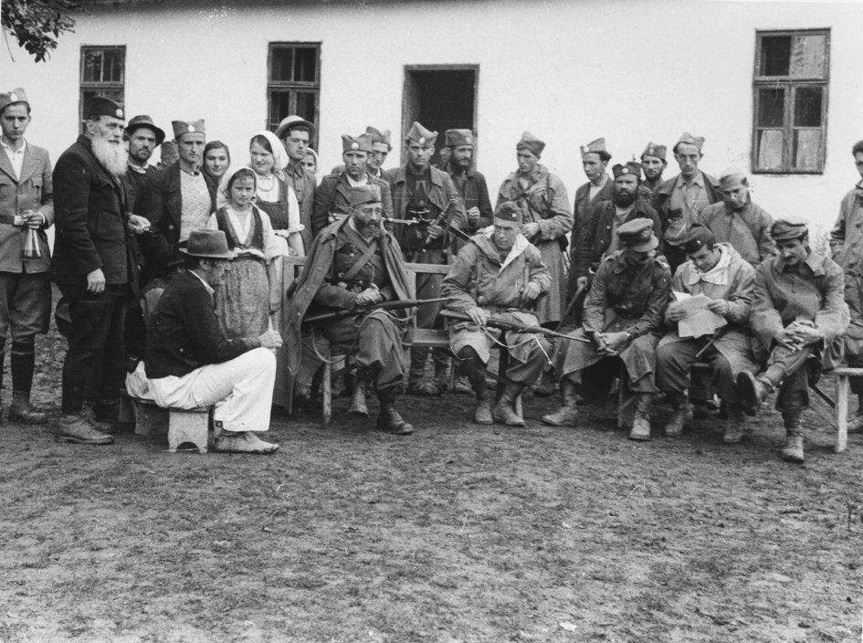 Dans la Possavina, en Bosnie, automne 1944. Le général Mihaïlovic et le colonel McDowell, assis, chacun un fusil sur les genoux, des civils, des Tchetniks et d'autres membres de la mission Alliée