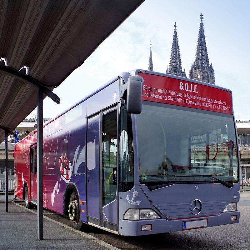 B.O.J.E. vor Kölner Dom Der Beratungsbus B.O.J.E. steht auf der Straße und ist im Dreiviertelprofil von vorne zu sehen. Hinter ihm sieht man die zwei Türme des Kölner Doms herausragen.