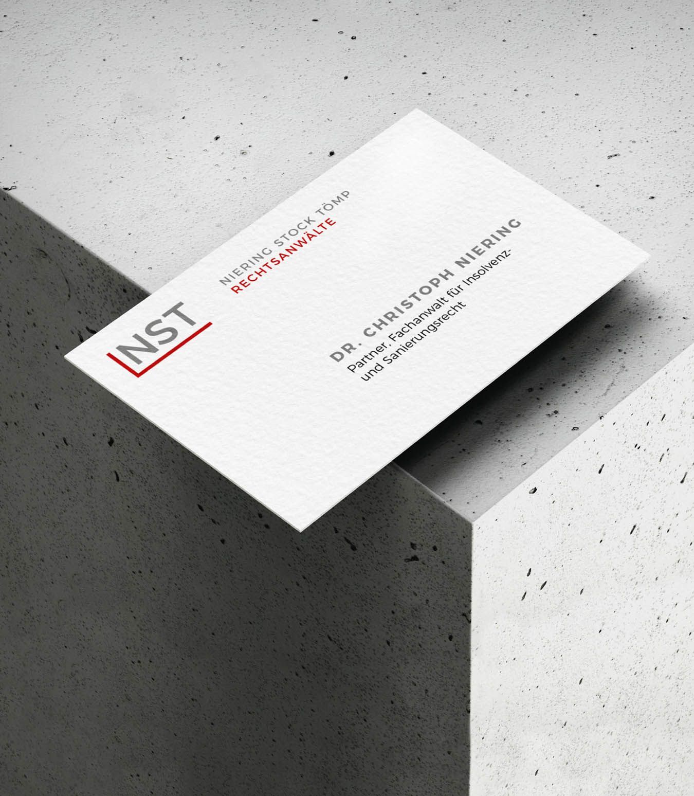 NST Visitenkarte NST Visitenkarte in gewinkelter, isometrischer Ansicht, liegend auf einem Betonwürfel.