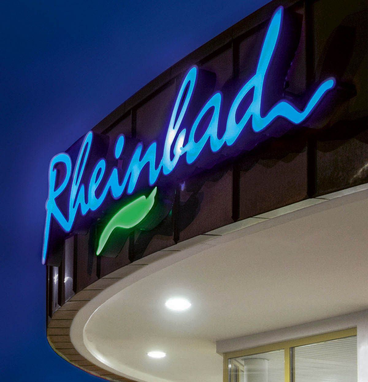Logo Rheinbad  Rheinbad Logo als Leuchtschrift auf der Überdachung in der Abenddämmerung blau-grün leuchtend