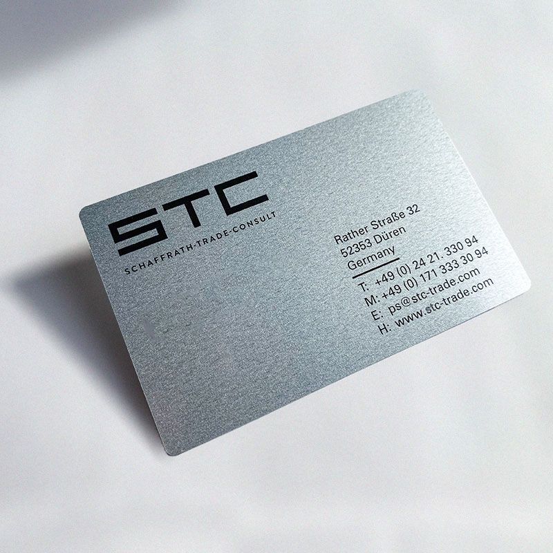 STC-Visitenkarte Visitenkarte aus Blech vor hellem Hintergrund. Der kantige Logoschriftzug „STC“ und die Adresse ist in schwarz aufgedruck .