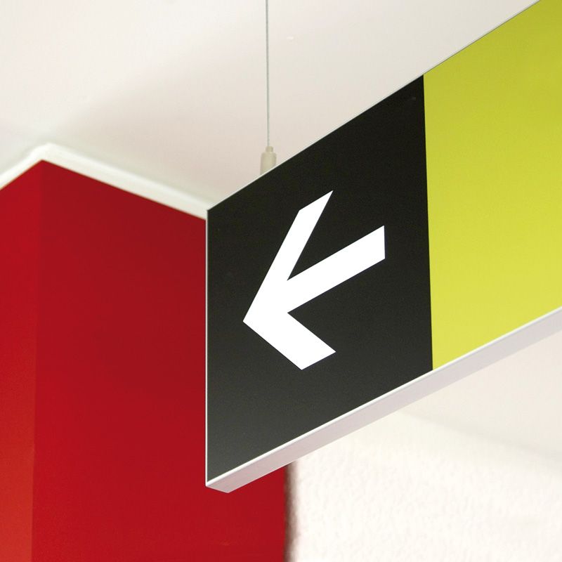 Schild mit Pfeil Wegeleitschild mit weißem Pfeil auf schwarzen Grund hängt an der Decke. Die Hintergrundwandfarbe ist rot und weiß.