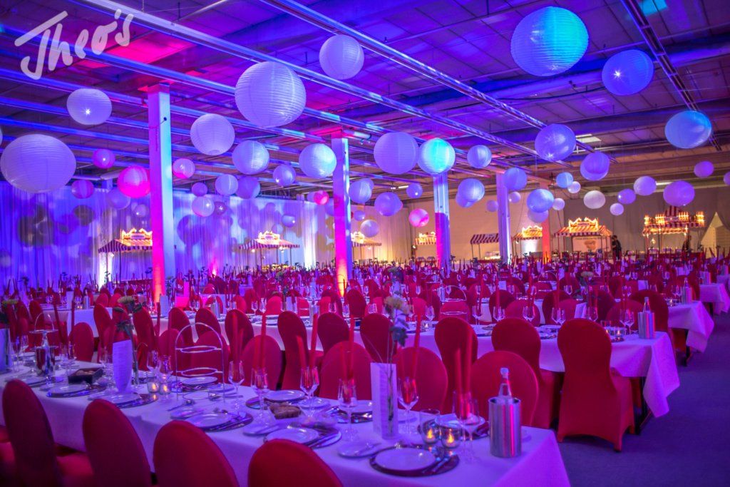 Event-Location dekoriert mit Luftballonen und in Reihen stehenden, festlich eingedeckten Tischen.