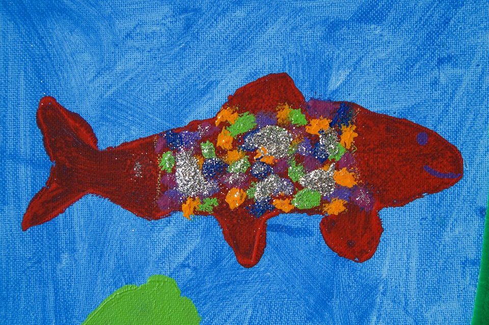 Tiere sind beliebte Motive bei kleinen Malerinnen und Malern. Ein gemalter bunter Fisch schwimmt durch das blaue Wasser.