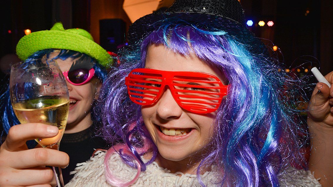 Let´s Party! Zwei Kinder mit Perücken und Sonnbrillen verkleidet, trinken Saft aus Sektgläsern.