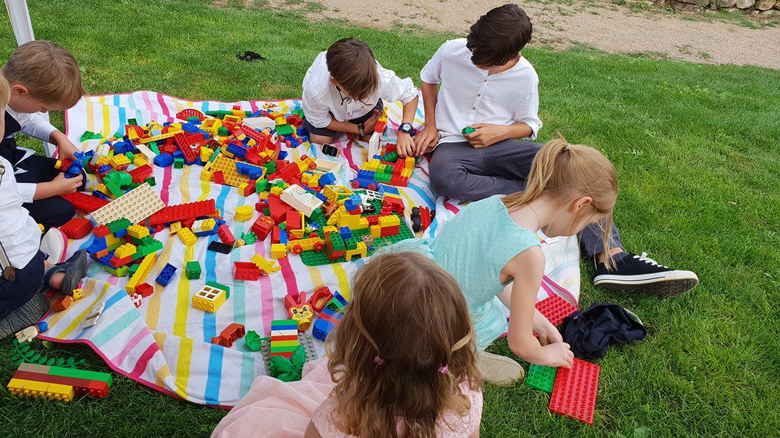 Kinder spielen Lego auf einer bunten Decke auf einer Wiese.