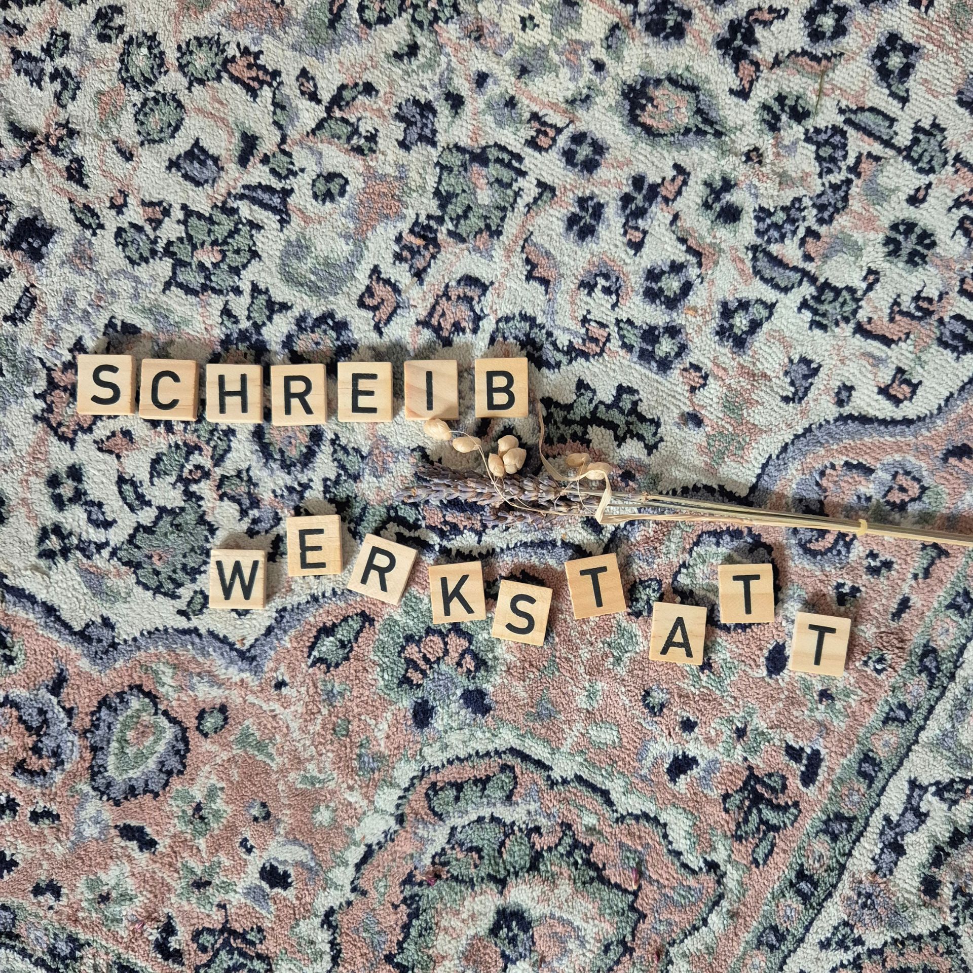 Alter Teppich, darauf Buchstaben aus Holz, die das Wort Schreibwerktstatt bilden.