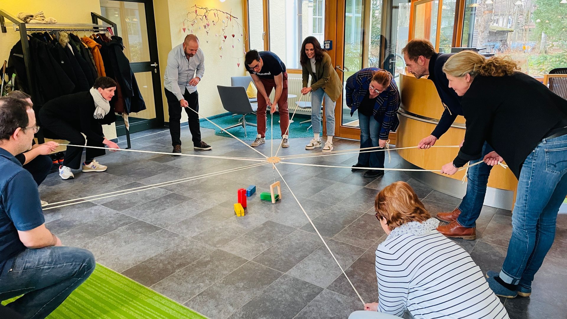 Seminarteilnehmer spannen Seile um Holzfiguren