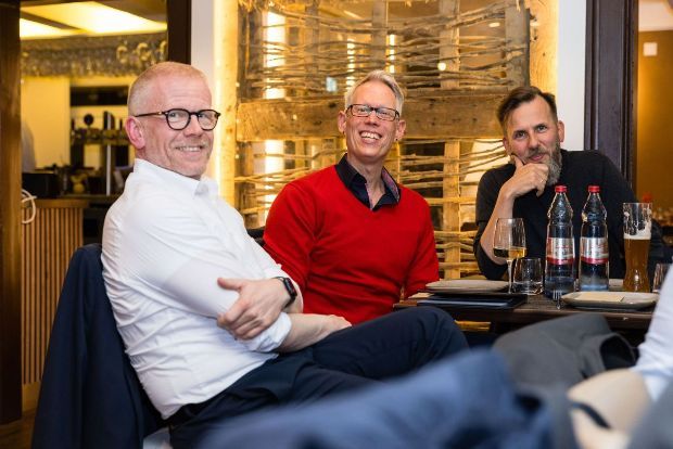 Drei Männer sitzen lächelnd an einem Restauranttisch.