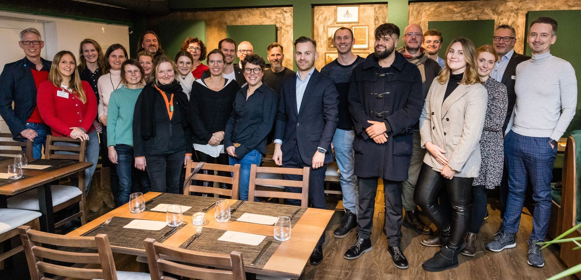 Eine Gruppe von Menschen verschiedener Geschlechter lächelt in einem warm beleuchteten Raum.