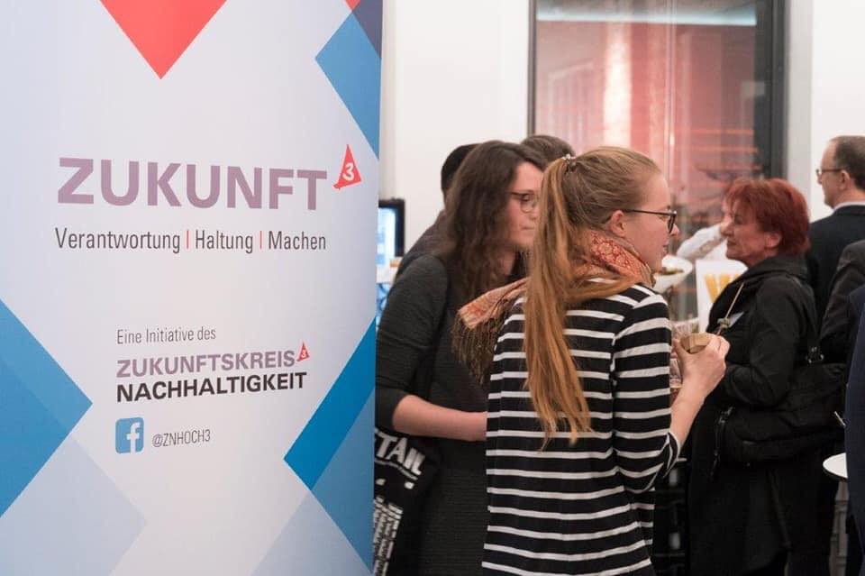 Eine Gruppe von Personen unterschiedlichen Geschlechts, die sich unterhalten und der ZNHoch3 Banner auf der linken Seite.