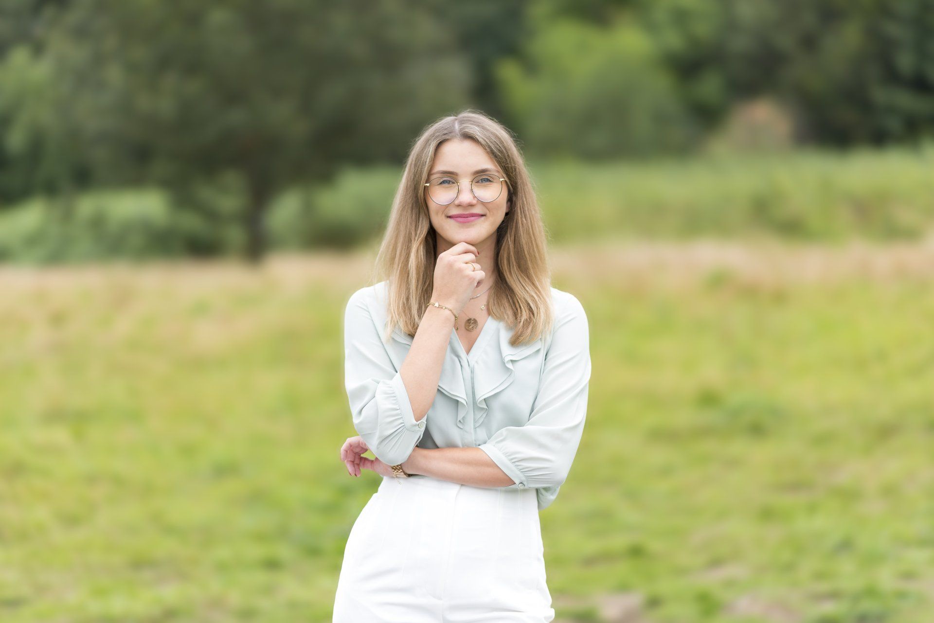 Eine Frau mit langen blonden Haaren und Brille steht auf einer grünen Wiese.