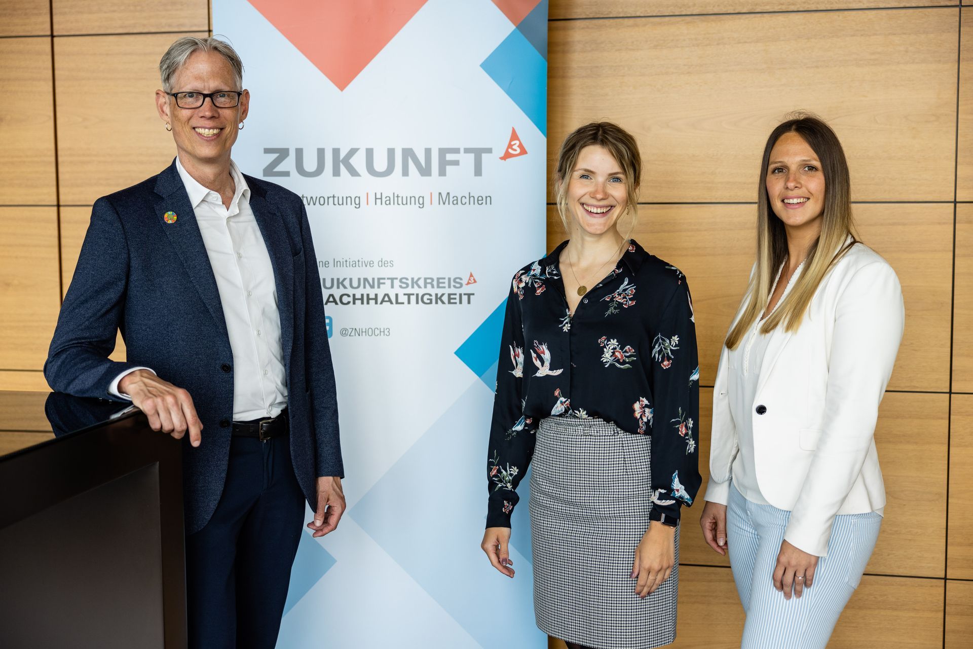 Zwei Frauen und ein Mann vor einem Werbebild des ZNHoch3