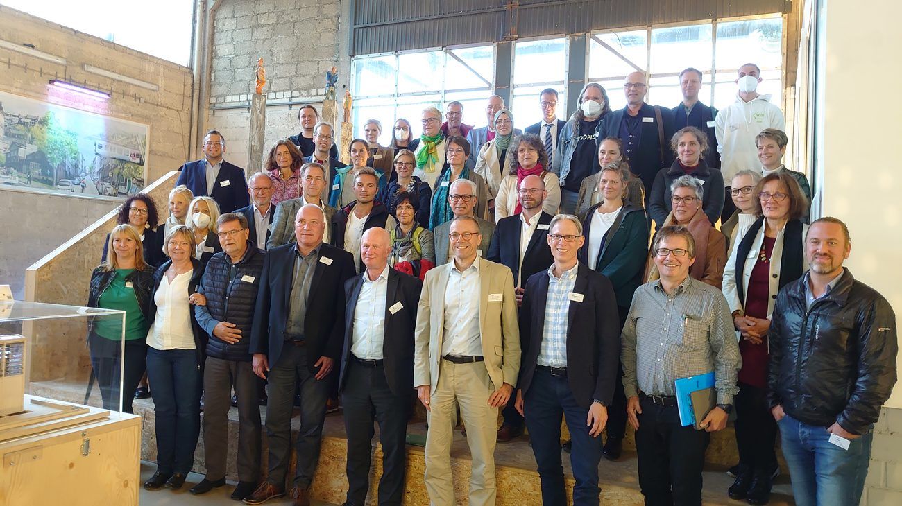 Eine große Gruppe von Menschen unterschiedlichen Geschlechts steht auf einer Treppe in einem Fabrikgebäude.