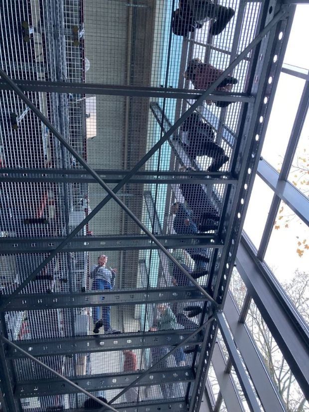 Blick von unten auf einen Metallsteg mit darüber gehenden Menschen.