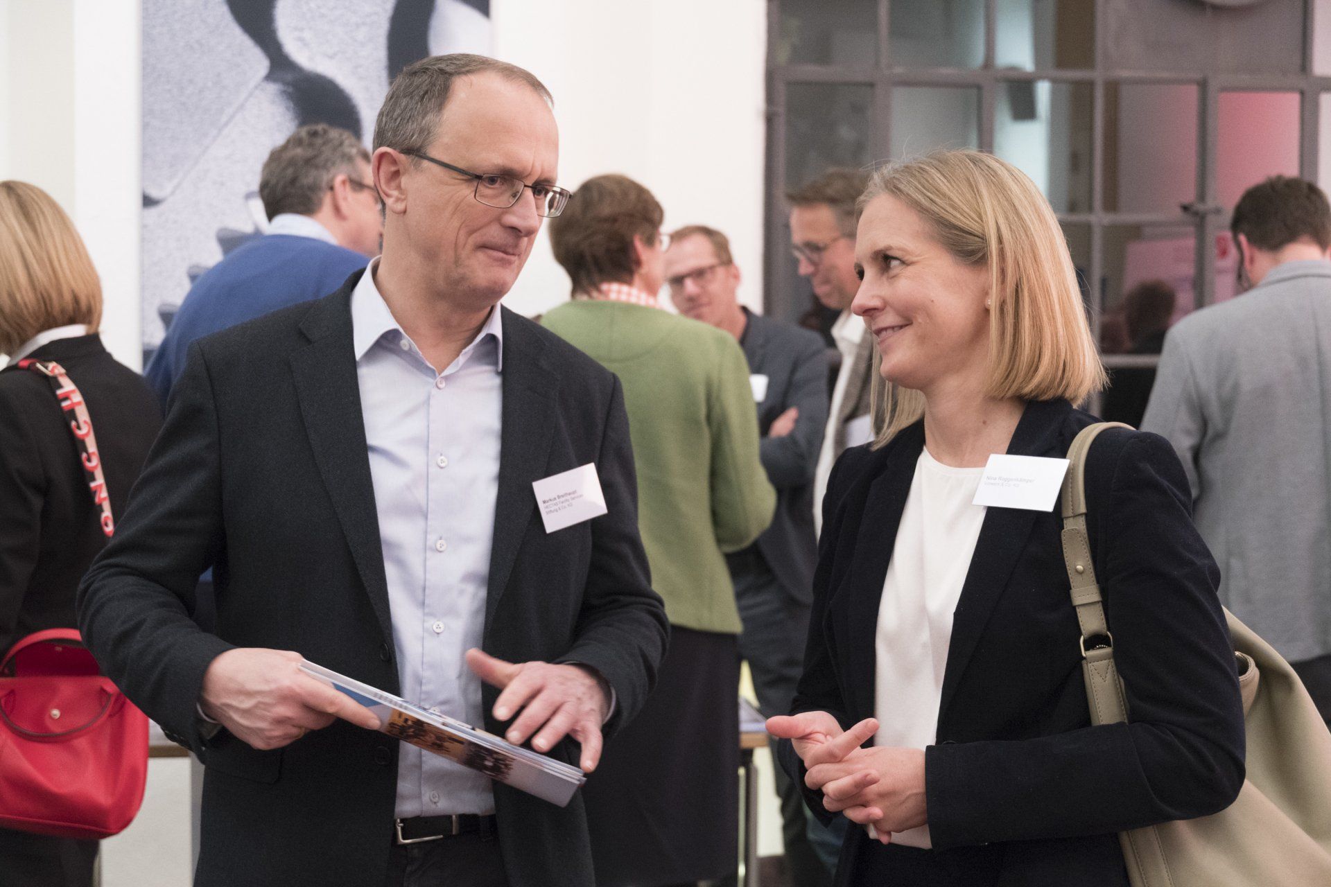 Ein Mann und eine Frau in Business-Kleidung unterhalten sich bei einer Veranstaltung.