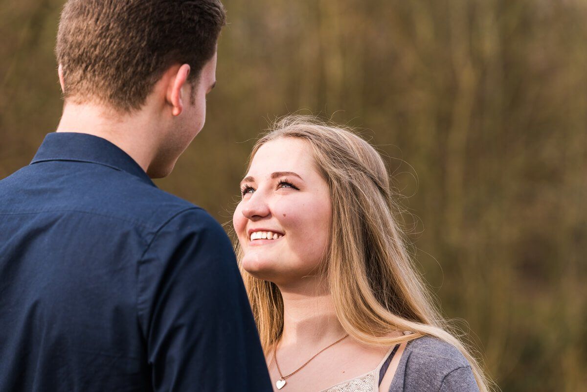 Portrait von einem jungen Paar draußen. Sie lächelt ihn an.