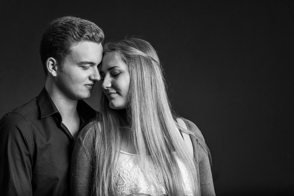 Ein Portrait von einem jungen Paar in schwarz-weiß. Die junge Frau steht mit dem Rücken an ihren Partner gelehnt und dreht sich leicht zu ihm.