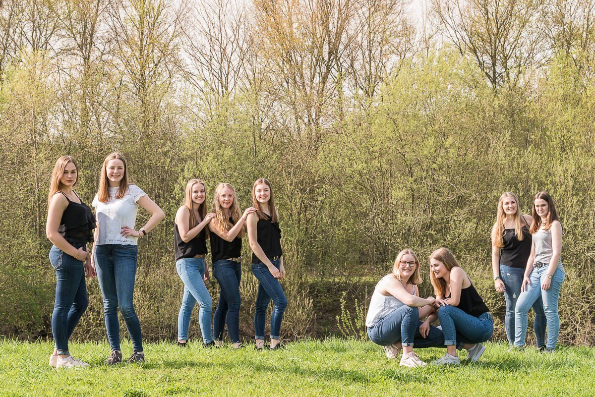 Neun junge Frauen, die sich auf einer grünen Wiese locker aufgestellt haben und in die Kamera lächeln.