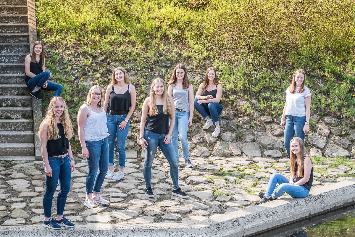 Neun junge Frauen in lockerer Aufstellung, die aus erhöhter Position fotografiert wurden.