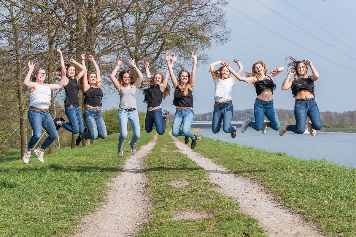 Neun junge Frauen springen am Dortmund-Ems-Kanal in Münster nebeneinander gleichzeitig in die Höhe und reissen dabei die Arme nach oben.