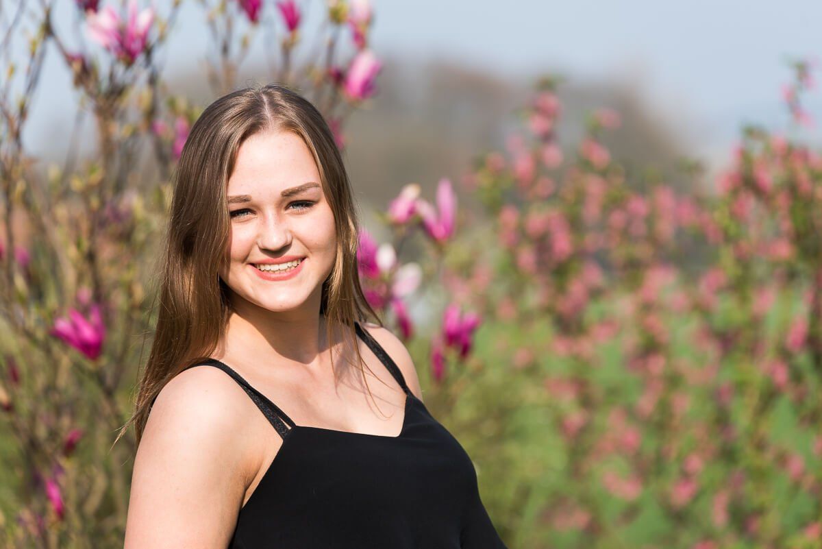 Ein Portrait einer lächelnden jungen Frau mit langen dunklen Haare im schwarzen Träger-Top in der Sonne.