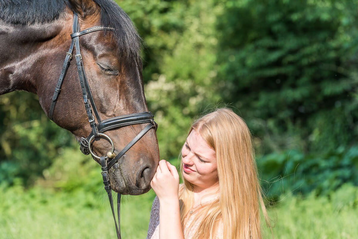 Junge Frau hockt vor ihrem Pferd und streichelt es an der Nase.