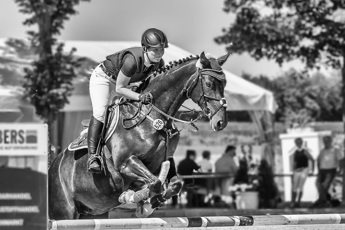 Eine Reiterin in schwarz-weiß, die auf einem Reitturnier in Münster mit ihrem Pferd über eine Hürde springt.