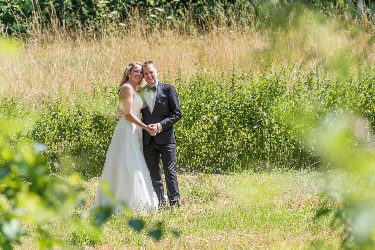 Ein Hochzeitspaar umarmt sich auf einer grünen Wiese. Die Braut trägt ein weißes Hochzeitskleid, der Bräutigam trägt einen schwarzen Smoking.