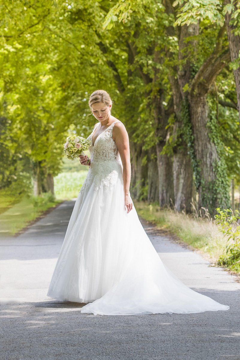 Ein Hochzeitspaar steht auf einer grünen Wiese. Die Braut trägt ein weißes Kleid, der Bräutigam trägt einen schwarzen Smoking.