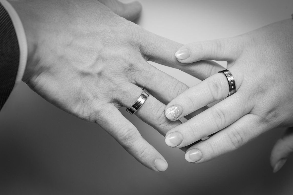 Ein Hochzeitspaar von hinten fotografiert im Wald. Sie gehen Hand in Hand. Die Braut trägt ein langes weißes Hochzeitskleid, der Bräutigam einen schwarzen Smoking.