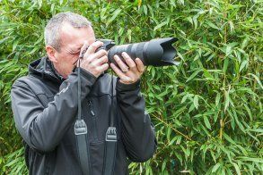 Carsten Pöhler fotografiert mit Kamera vor grünem Bambus.