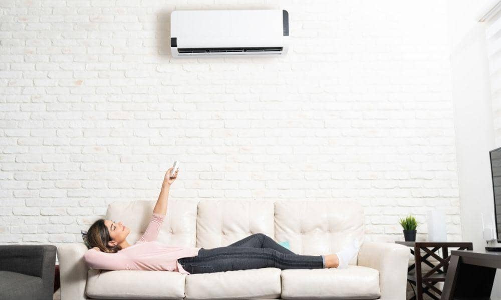 woman on couch holding remote control for ductless mini split ac unit