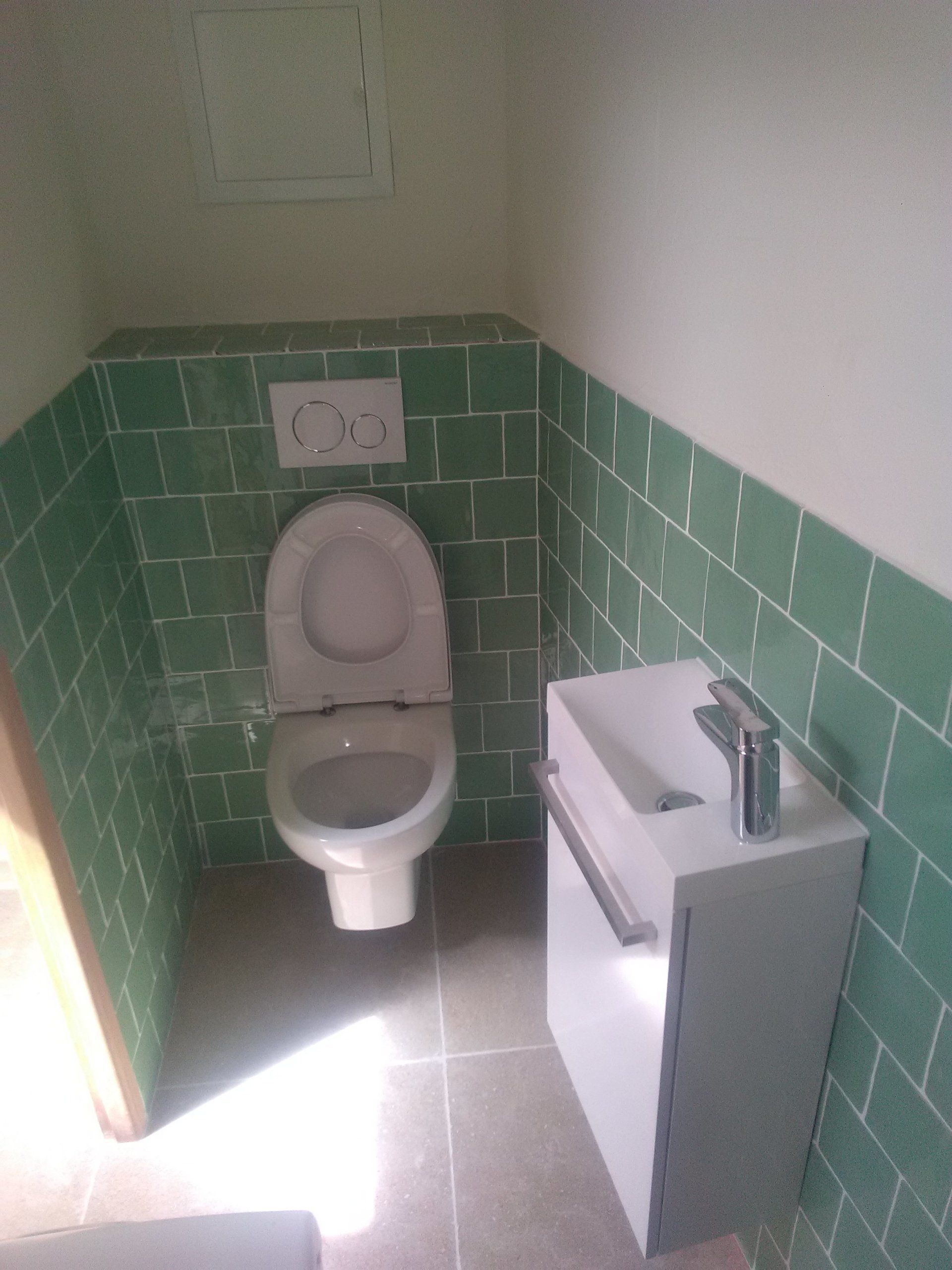 toilettes et lavabo dans une salle blanche et carrelée de vert