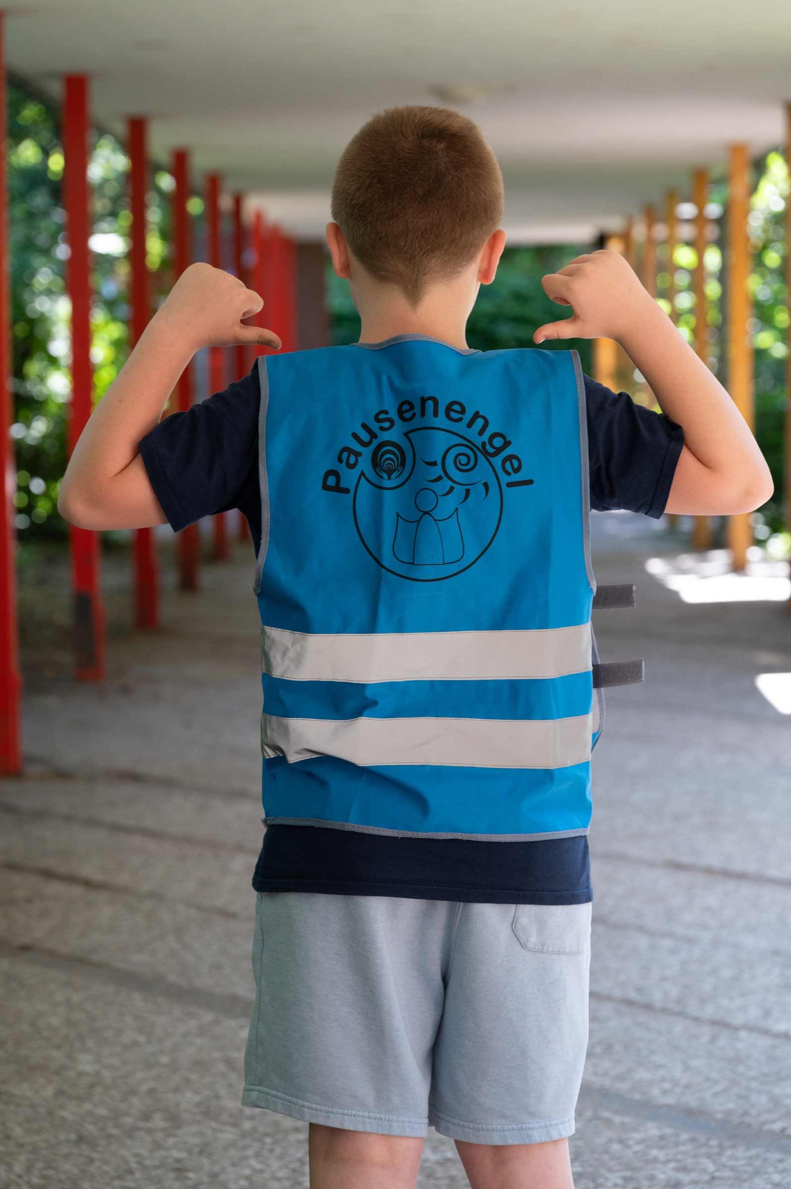 Schulfotografie Hamburg – ein Schülerlotse zeigt auf sein Shirt, Symbolbild zu den FAQs