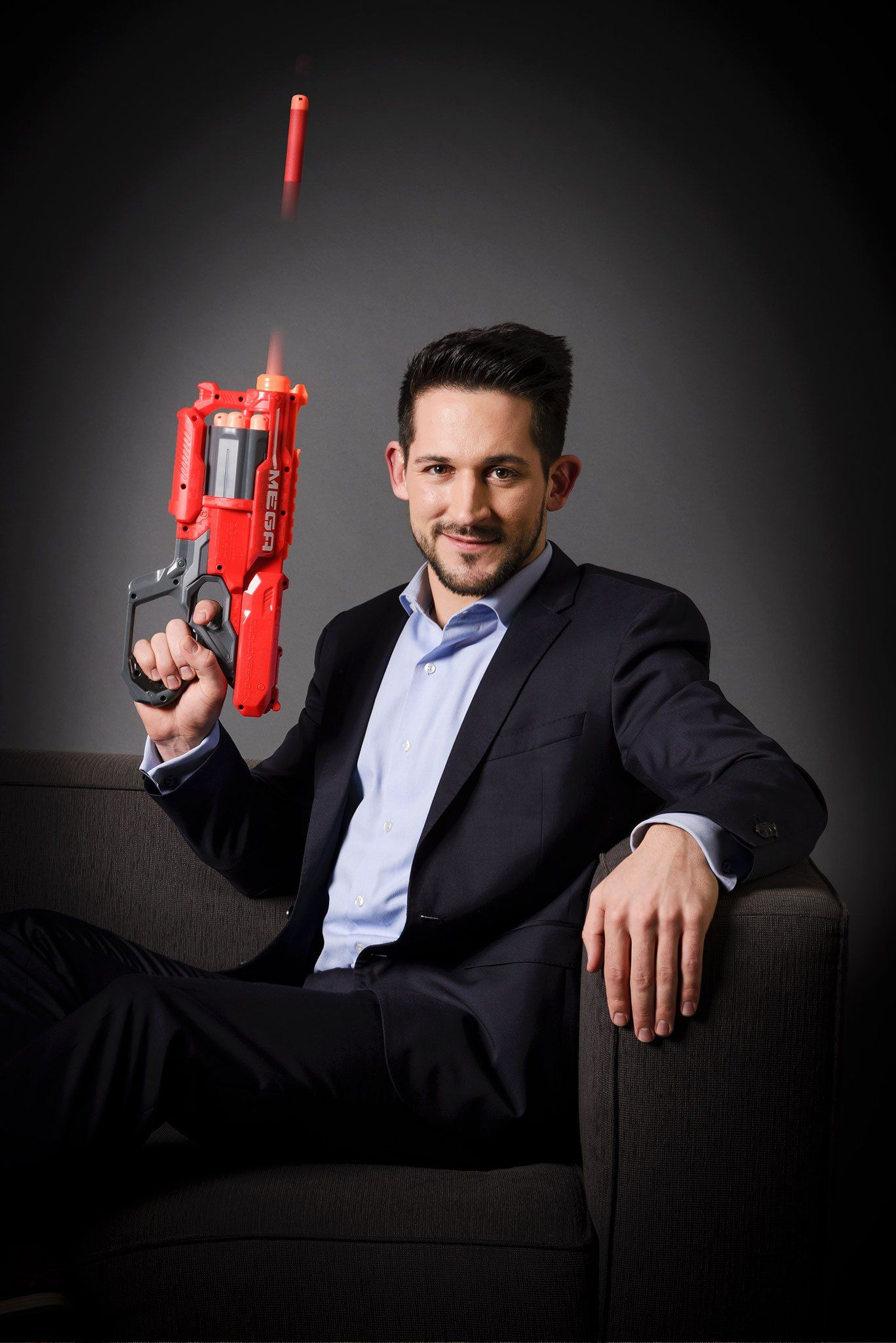 Ein Manager mit einer roten Kinderpistole auf einem Sofa sitzend, Businessfotografie aus Hamburg von Kay Winter / WINTERPOL
