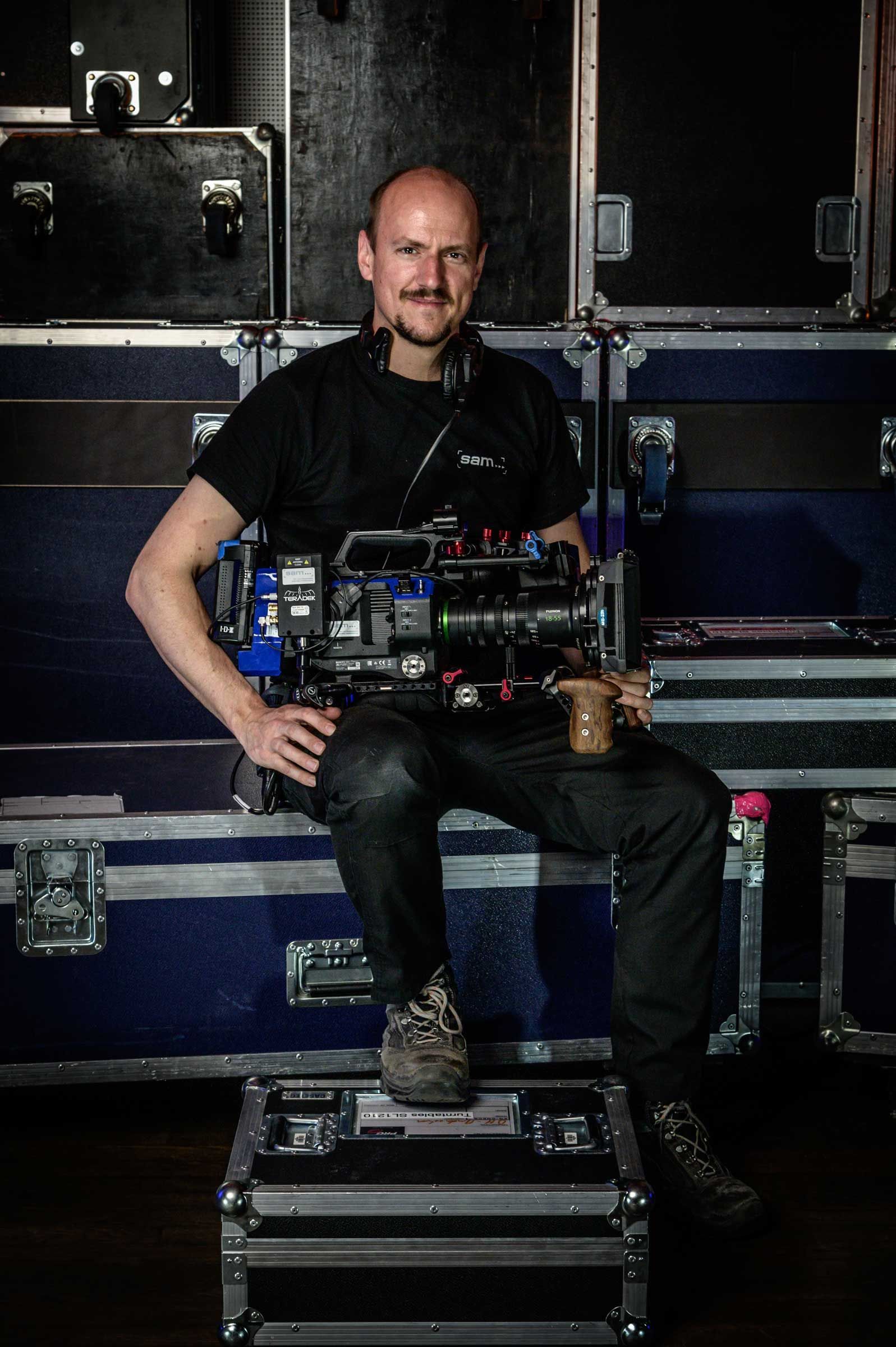 Ein Kameramann von SAM-Medien sitzt auf diversen Cases, Businessfotografie aus Hamburg von Kay Winter / WINTERPOL Ein Kameramann sitzt auf diversen Cases.
