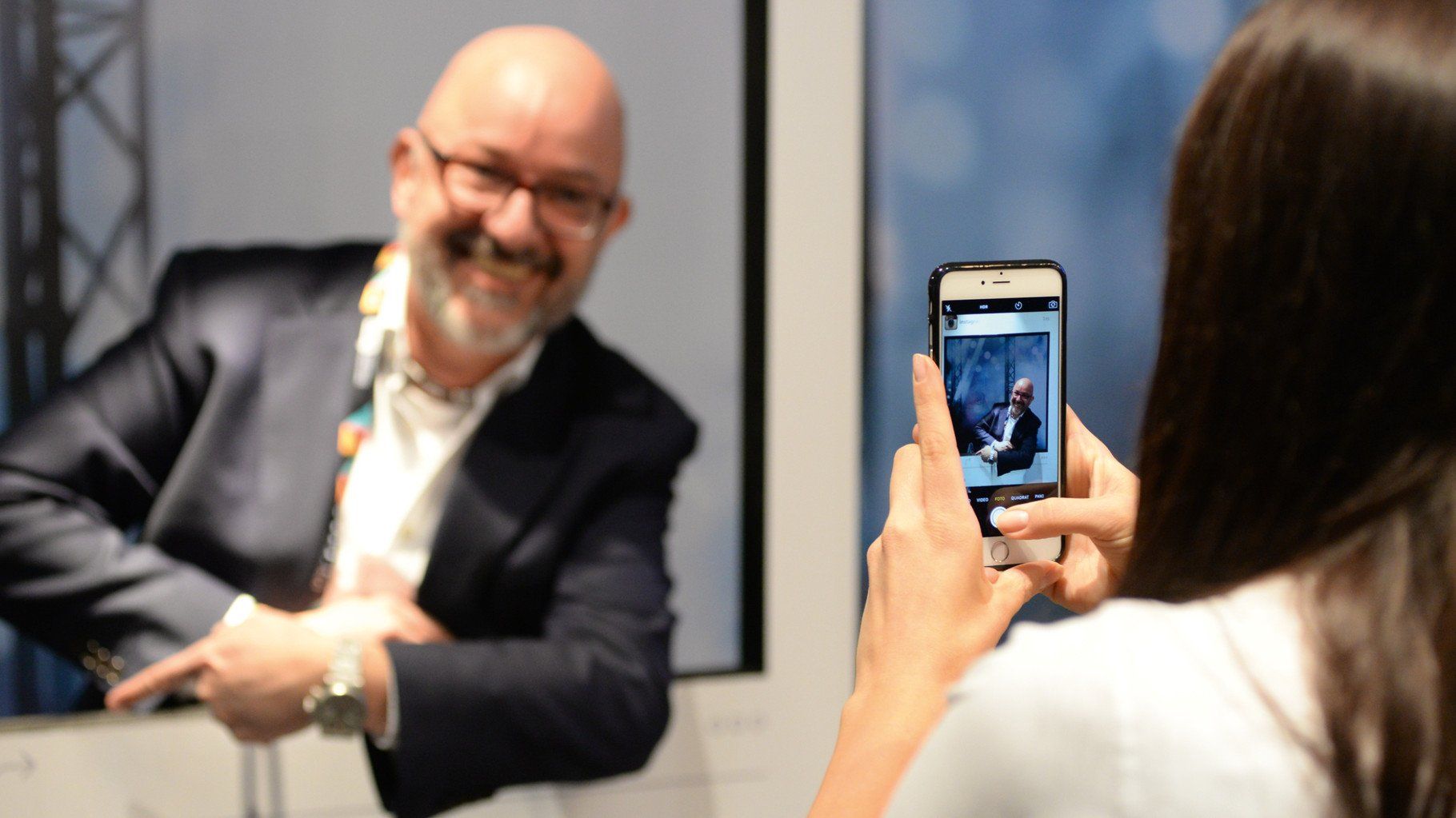 Ein Mann mit Glatze, Brille und Bart wird von einer jungen Frau mit dem Handy fotografiert, Eventfotografie aus Hamburg von Fotograf Kay Winter / WINTERPOL