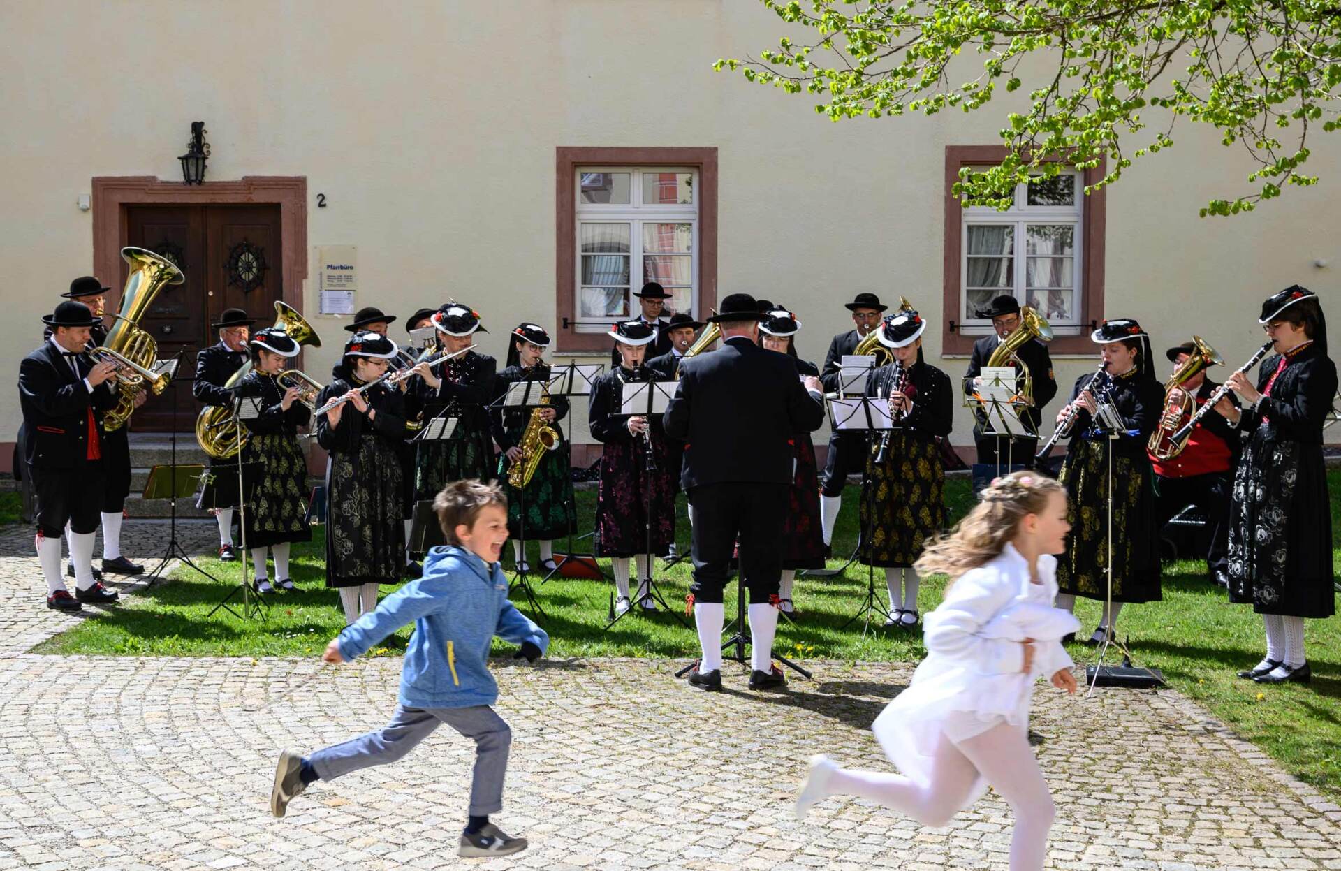Ein Blasorchester spielt im Hof eines historischen Gebäudes im Schwarzwald, davor laufen zwei Kinder – Reise-Fotografie von WINTERPOL Hamburg