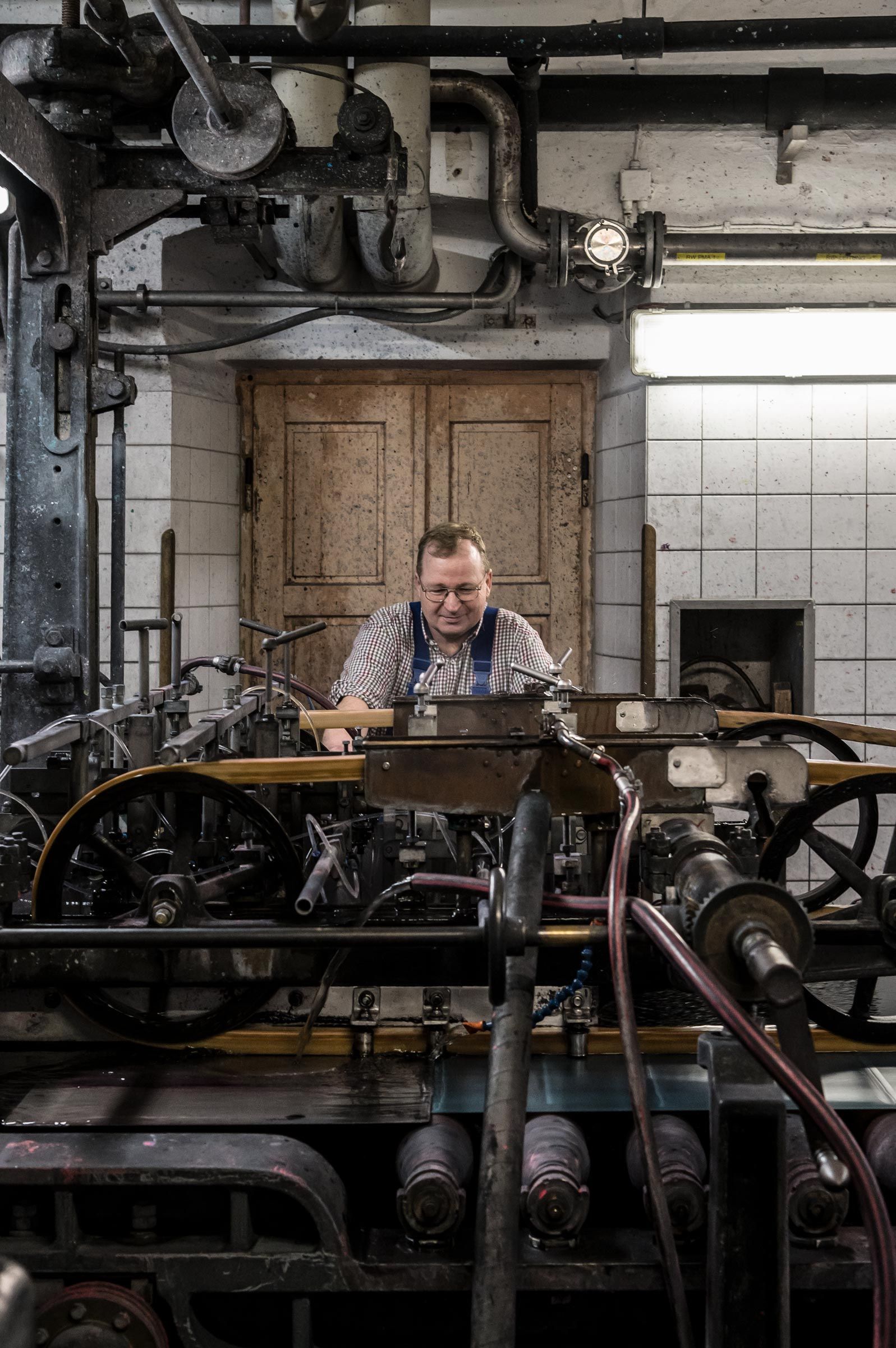 In der Papierfabrik Gmund arbeitet ein Techniker an der alten Druckmaschine  – Reportage-Fotografie von WINTERPOL Hamburg
