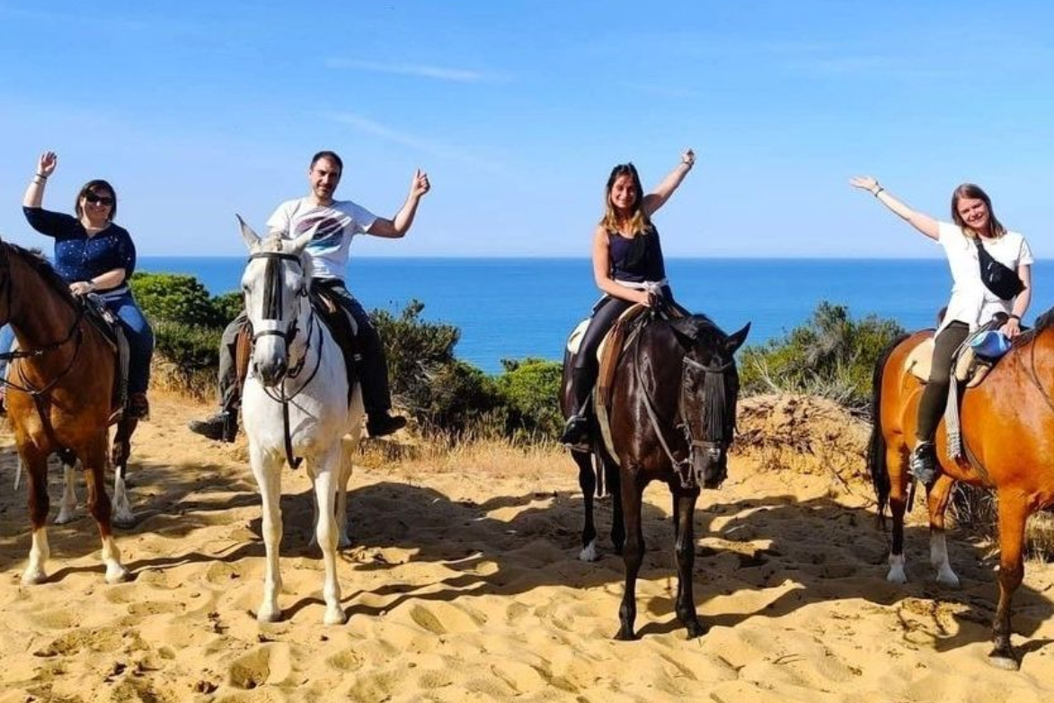 Group of riders on a dune with the Atlantic in the background. Horse riding routes in Doñana, Spain.