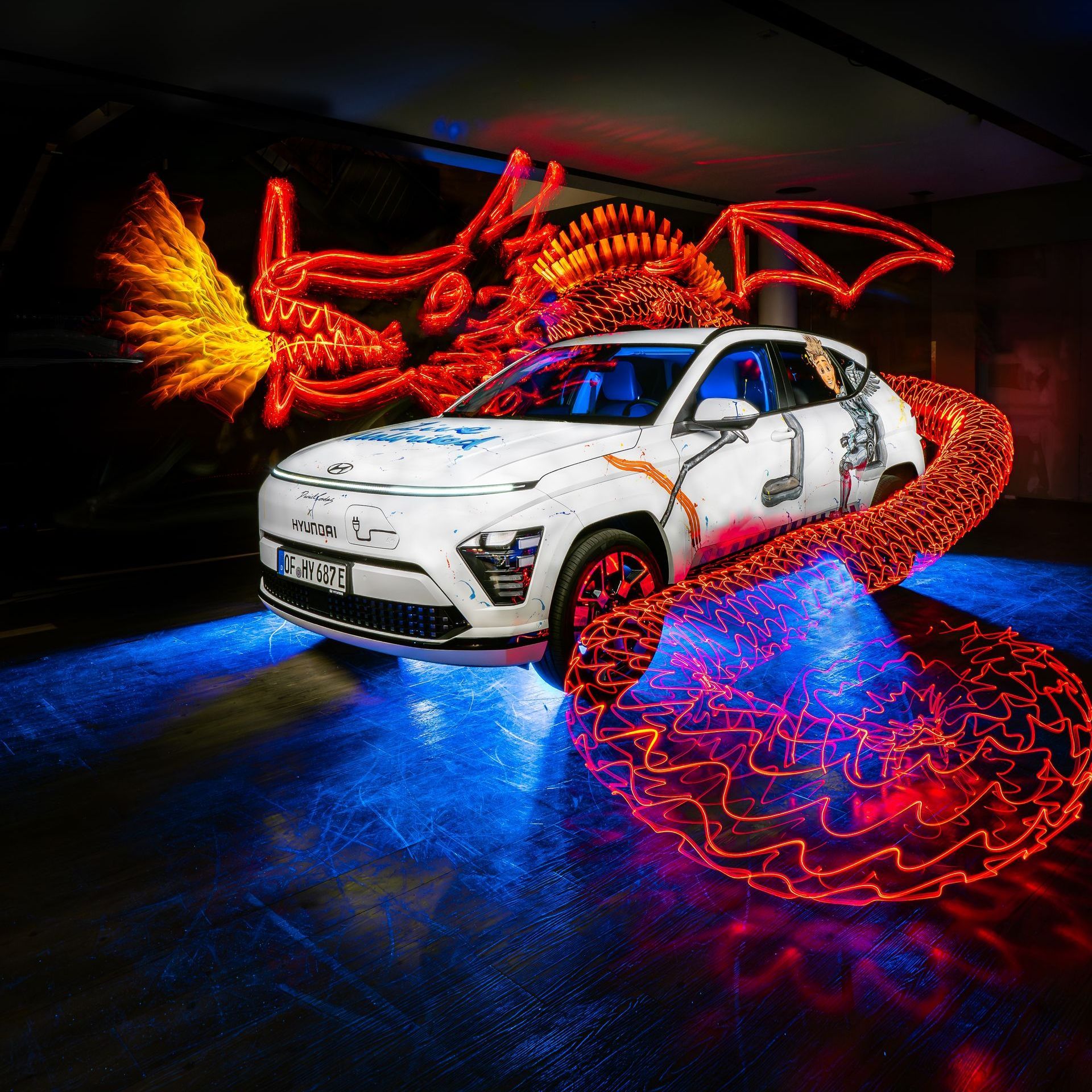 Das Bild zeigt ein Lightpainting mit einem Auto. Bei dem Lightpainting handelt es sich um einen aus Licht gemalten Drachen, der sich um das Auto windet und Feuer spuckt.