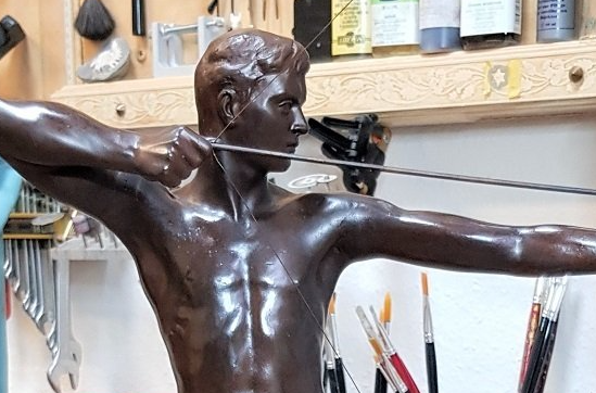 Der Arm wurde mit einer speziellen Modelliermasse modelliert und in Wachsschmelz-Verfahren in Bronze gegossen. Bogen und Pfeil wurden aus Bronze-Profilen geformt und angepasst. Den Sockel haben wir in diesem Fall aus schwarzem Granit angefertigt.