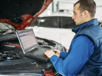 Mann mit Computer arbeitet an einem Kfz Motor