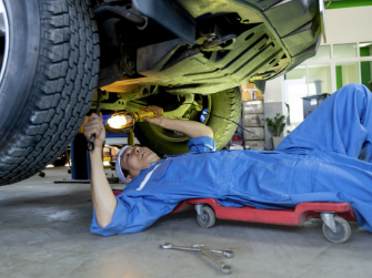 Man liegt auf einem Rollbrett und begutachtet einen SUV von unten.