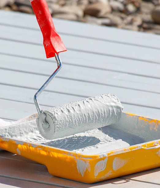 An individual is using a paint roller to coat the exterior wall of a home with fresh paint.