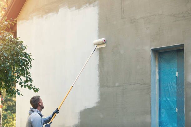 A man painting the exterior of a house with a roller, focused on applying a fresh coat of paint.